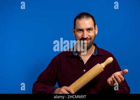 Close-up of Hispanic man with malicious look trying to attack you with a rolling pin - isolated on blue background. Stock Photo