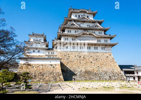 The Renketsushiki (compound) keep of the white Himeji castle keep against a clear blue sky. In foreground roped walkway holding areas for busy times. Stock Photo