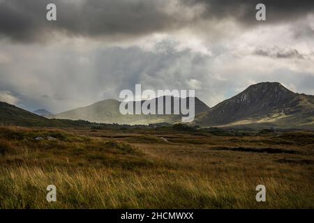 Sunbeams break through the dark clouds over the green sloping mountains of Connemara national park in County Galway in Ireland. A remote area. Stock Photo