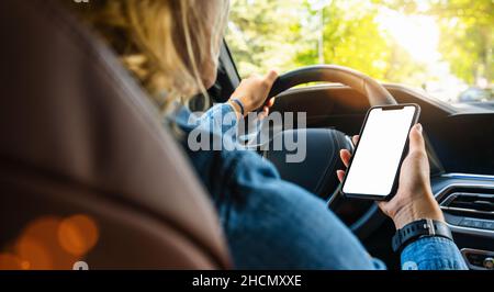 Woman holding black mobile phone in hands with blank desktop screen while car driving at summer in the city, Mockup image Stock Photo