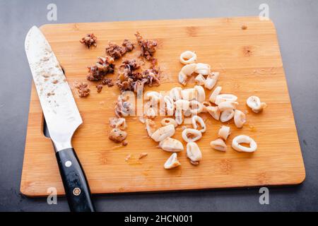Cooked Squid Tubes Cut into Rings on a Bamboo Cutting Board: Cooked squid tubes and tentacles on a wooden cutting board Stock Photo