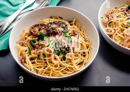 Overhead View of Squid Piccata Garnished with Charred Lemon Slices: Bowls of squid piccata made with linguine pasta noodles Stock Photo