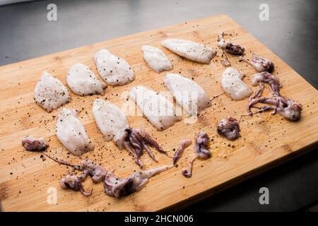 Raw Squid Tubes and Tentacles Seasoned with Salt and Pepper: Uncooked squid on a bamboo cutting board Stock Photo