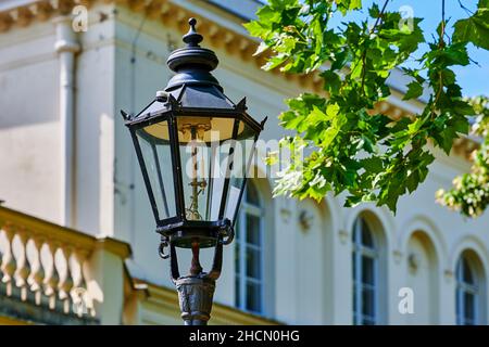 View to the top of an old gas lantern in front of a blurred historic building. Stock Photo