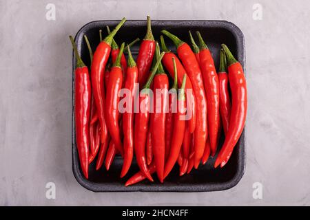 Whole ripe red hot chili peppers in black plastic tray on background with imitation of plaster of paris. Selective focus. Stock Photo