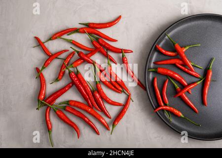 A whole ripe red hot chilli next to black plate on stucco textured surface. Selective focus. Stock Photo