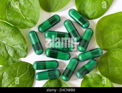 Green supplement capsules with spinach leaves on white. Stock Photo