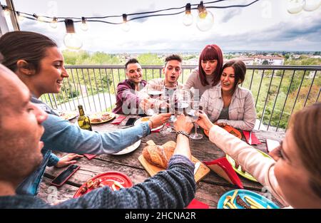 Wide angle view of happy people toasting red wine together at rooftop party in open air villa - Young friends eating bar-b-q food at restaurant patio Stock Photo