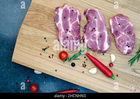 Three juicy steaks lie next to red and green chili peppers, a sprig of rosemary and garlic on a wooden table. Stock Photo
