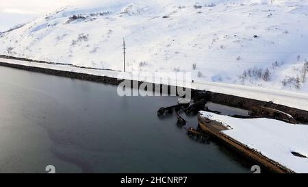 Aerial view of winter snowy sea coast with ruined boats after the shipwreck. Old sunken fishing boats on the shore of the Barents Sea. Stock Photo