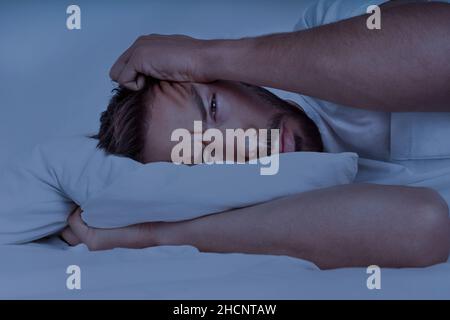 Young man lying in the bed and trying to sleep, can't sleep. Man suffering from insomnia, sleeping problems or sleep disorders. Stock Photo