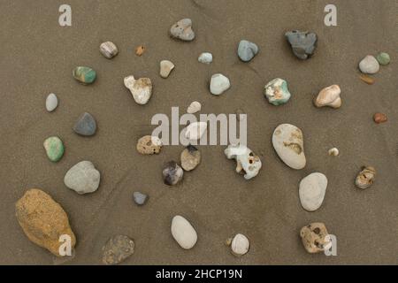Top view of a group of stones of different colors and textures on an empty beach during the day Stock Photo