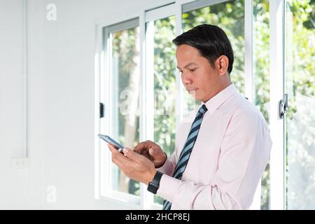 a business man standing by the window using a mobile phone Stock Photo