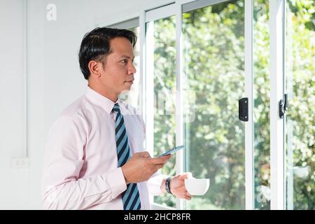 a business man standing by the window using a mobile phone Stock Photo