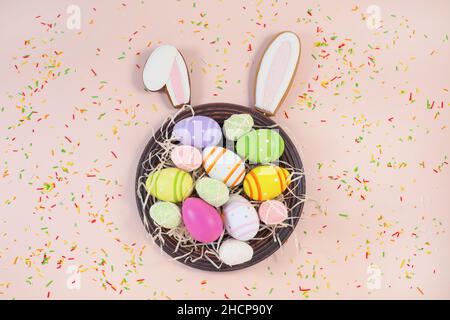 Gingerbread easter bunny ears and painted easter eggs on plate and sweet color sprinkles on a pink background. Sweets for celebrating Easter. Stock Photo