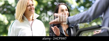 Young women and man in wheelchair laugh and chat in park Stock Photo