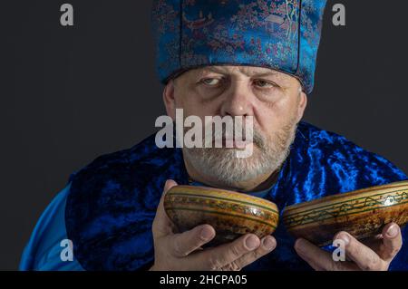 Nice portrait of bearded senior man in blue oriental clothes drinking tea from two saucers Stock Photo