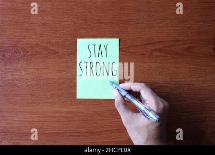 Top view image of paper with text STAY STRONG and hand holding pen. Stock Photo
