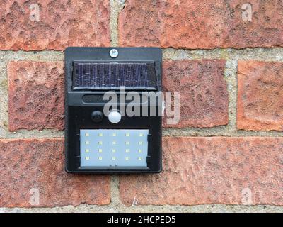 A solar powered motion sensor light with a LED array fixed to a brick wall Stock Photo
