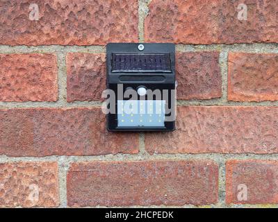 A solar powered motion sensor light with a LED array fixed to a brick wall Stock Photo