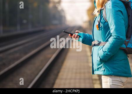 Woman using her smartphone while waiting for a train. Tourist is buying ticket online by mobile phone. Travel concept Stock Photo