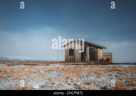 Cosy log cabin retreat in snow covered landscape, Iceland, Europe. Iceland nature with typical yellow grass and snow mountains in the eastfjords. Stock Photo