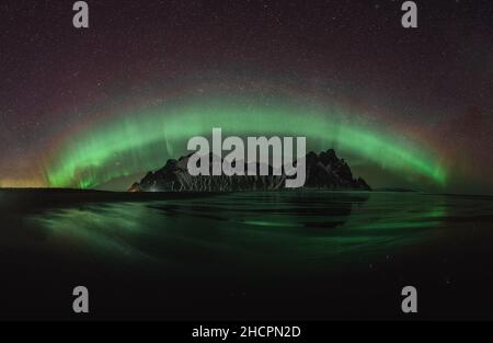 Vestrahorn Stockknes mountain range with aurora borealis and reflection at the beach in Iceland. One of the most beautiful famous nature heritage in Stock Photo