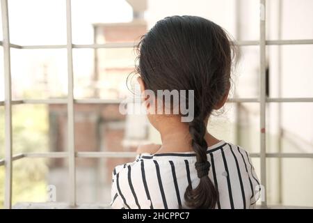 sad child kid girl looking through window  Stock Photo