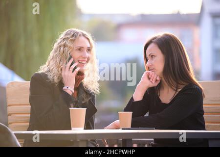 Unhappy young woman waiting angrily while her friend is talking happily on sellphone with someone else and ignoring her. Friendship problems concept. Stock Photo
