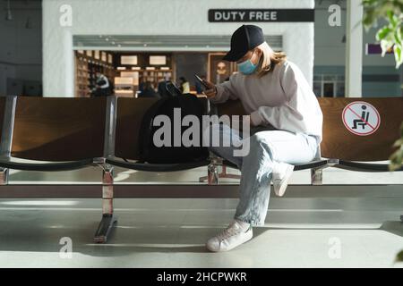 Casual young girl in mask with smartphone in airport lounge. Air travel under quarantine conditions Stock Photo