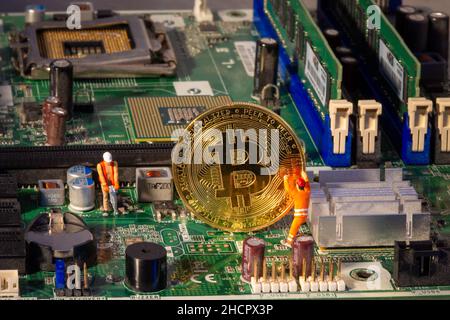 Bitcoin mining inside a computer. Two small Bitcoin miners figurines extracting valuable electronically-mined digital cryptocurrency from motherboard Stock Photo