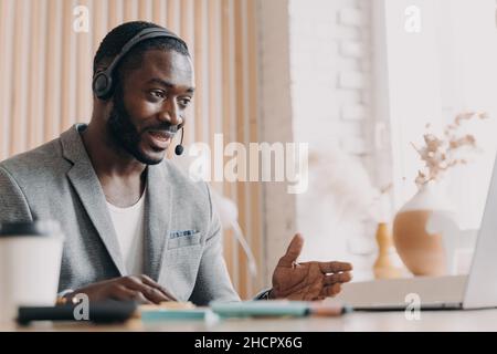 Young smiling african american man in headset consulting client customer via video call on laptop Stock Photo