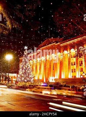 Cars on road in traffic on rush hours at night in rustaveli avenue in capital city Tbilisi in Georgia on Christmas with xmas tree by parliament on bac Stock Photo