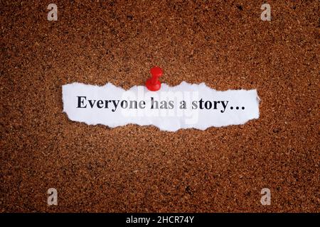 A piece of paper with the words Everyone has a story written on it that is pinned to a cork board. Close up Stock Photo