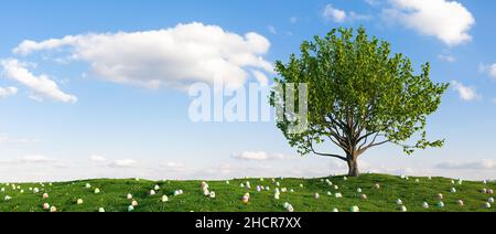 Many colorful Easter eggs lie in the grass of a meadow with tree for Easter Stock Photo