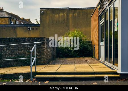Street view from a terrace of an entrance of a building with bush, metallic railings, brick wall Stock Photo