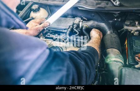 car service, repair, maintenance and people concept - auto mechanic man with lamp working at workshop Stock Photo