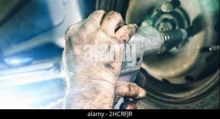 Mechanic changing a car tire in a workshop on a vehicle on a hoist using an electric drill to loosen the bolts in a concept of service or replacement Stock Photo