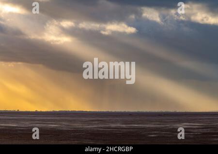 crepuscular or sun rays breaking through clouds over sea at RSPB snettisham and the wash on the north norfolk coast in autumn, bright rays of light, Stock Photo