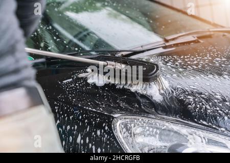 Man washes a car with brush. Carwash. Washing machine at the station Stock Photo