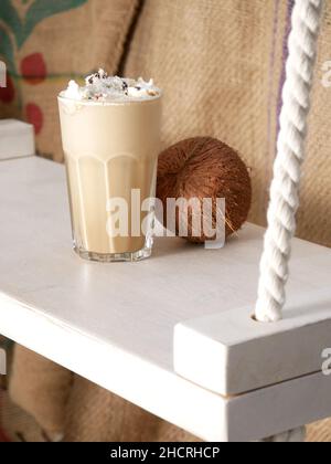 Coconut latte in a tall glass and coconut on a swing in a cafe. Close up. Stock Photo