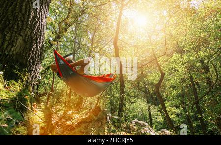 man relaxing in the hammock hanging among the trees in the forest Stock Photo