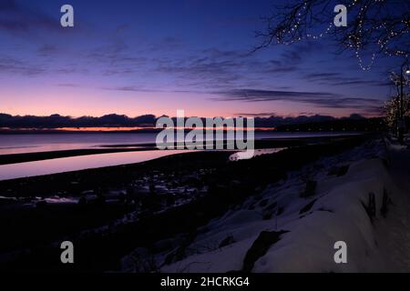 Sunset silhouettes mountains of Vancouver Island along the horizon from White Rock, BC's snow-covered waterfront. Stock Photo