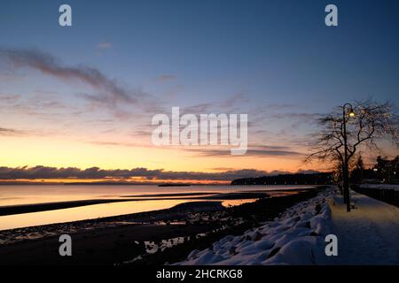 Quiet waterfront promenade in White Rock, BC, after a snowfall.  Lights sparkle on trees and along the pier. Stock Photo