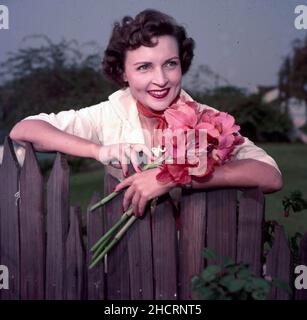 Circa 1957, Hollywood, California, USA: American actress and comedian BETTY WHITE leaning or garden fence holding fresh picked red flowers. (Credit Image: © Globe Photos/ZUMA Press Wire) Stock Photo