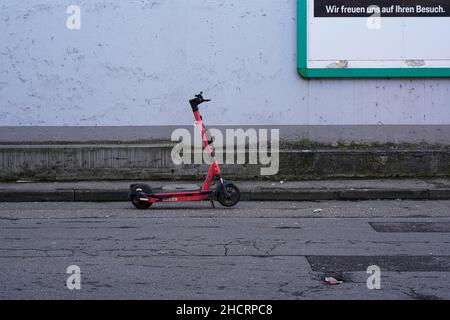 A red electric scooter parked by the roadside in front of a wall. Stock Photo