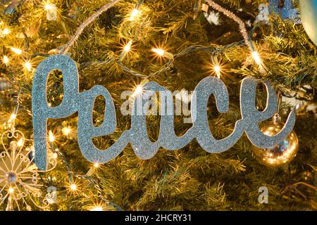 Peace sign hanging as a Christmas tree decoration surrounded by twinkling lights and warm moody lighting. Stock Photo