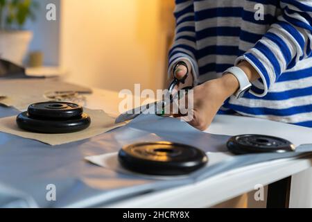 Clothing designer cut fabric using scissors and weights. Sewer working on fashion clothes in studio Stock Photo