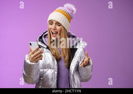 Bothered complaining dissatisfied cute blond girl yelling stupid smartphone standing unhappy recording audio message whining yelling mobile phone Stock Photo