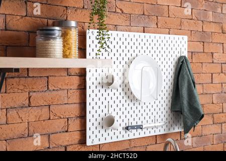 Peg board with kitchenware hanging on brick wall Stock Photo